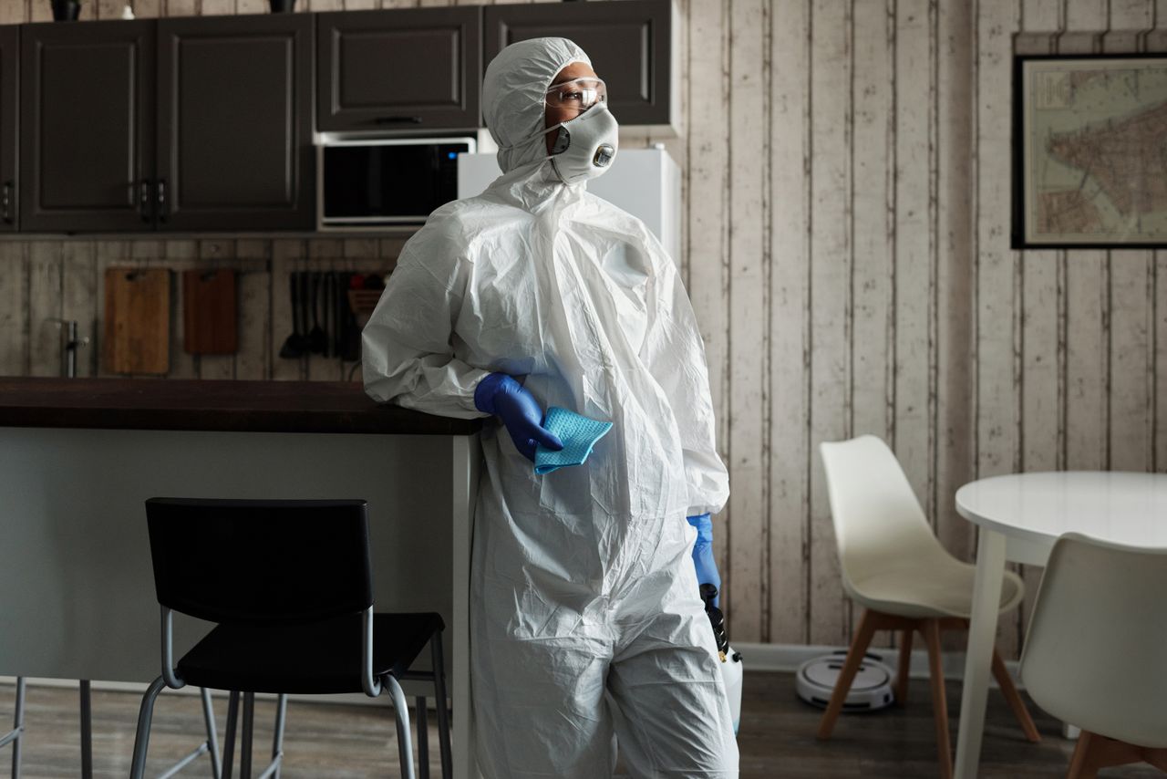 A person in full PPE gear standing indoors, emphasizing disinfection during COVID-19.